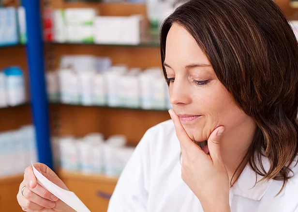 Apothekerin schaut nachdenklich auf ein Rezept