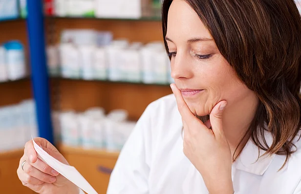 Apothekerin schaut nachdenklich auf ein Rezept